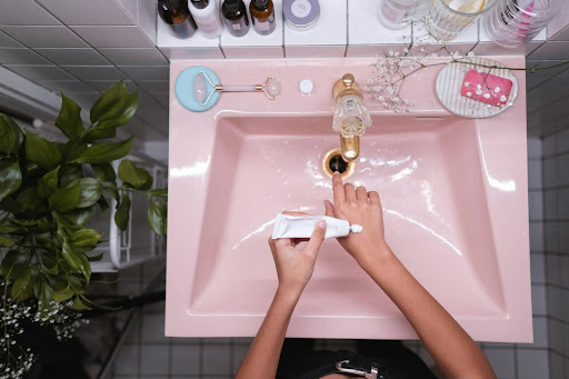woman putting cream on her hands over pink bathroom sink